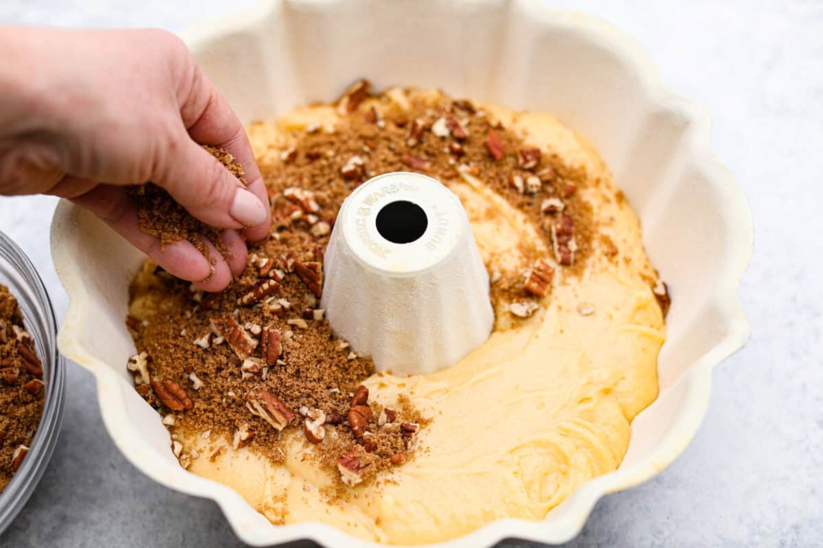 Overhead shot of someone sprinkling the pecan mixture over the sock it to me cake batter in the bottom of the bundt pan. 