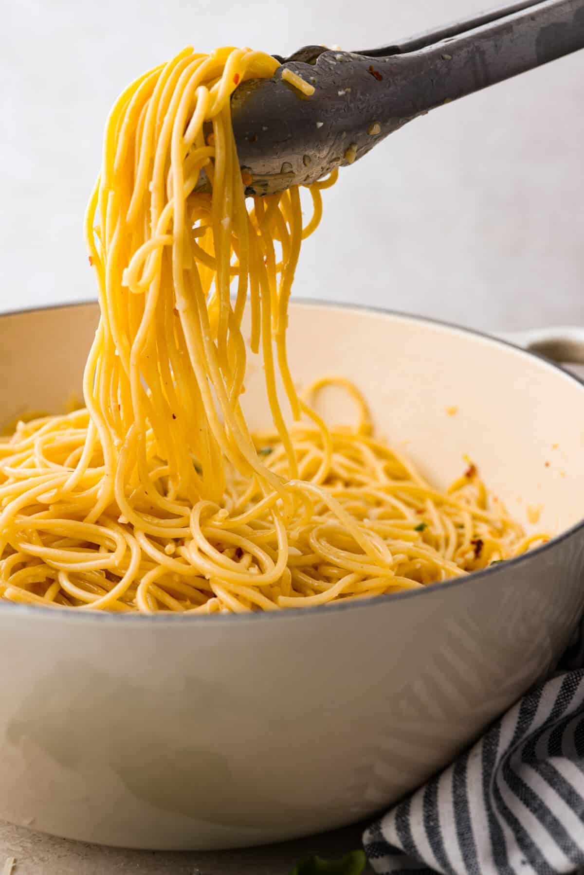 Side shot of someone lifting some of the spaghetti aglio e olio from the pot with tongs. 