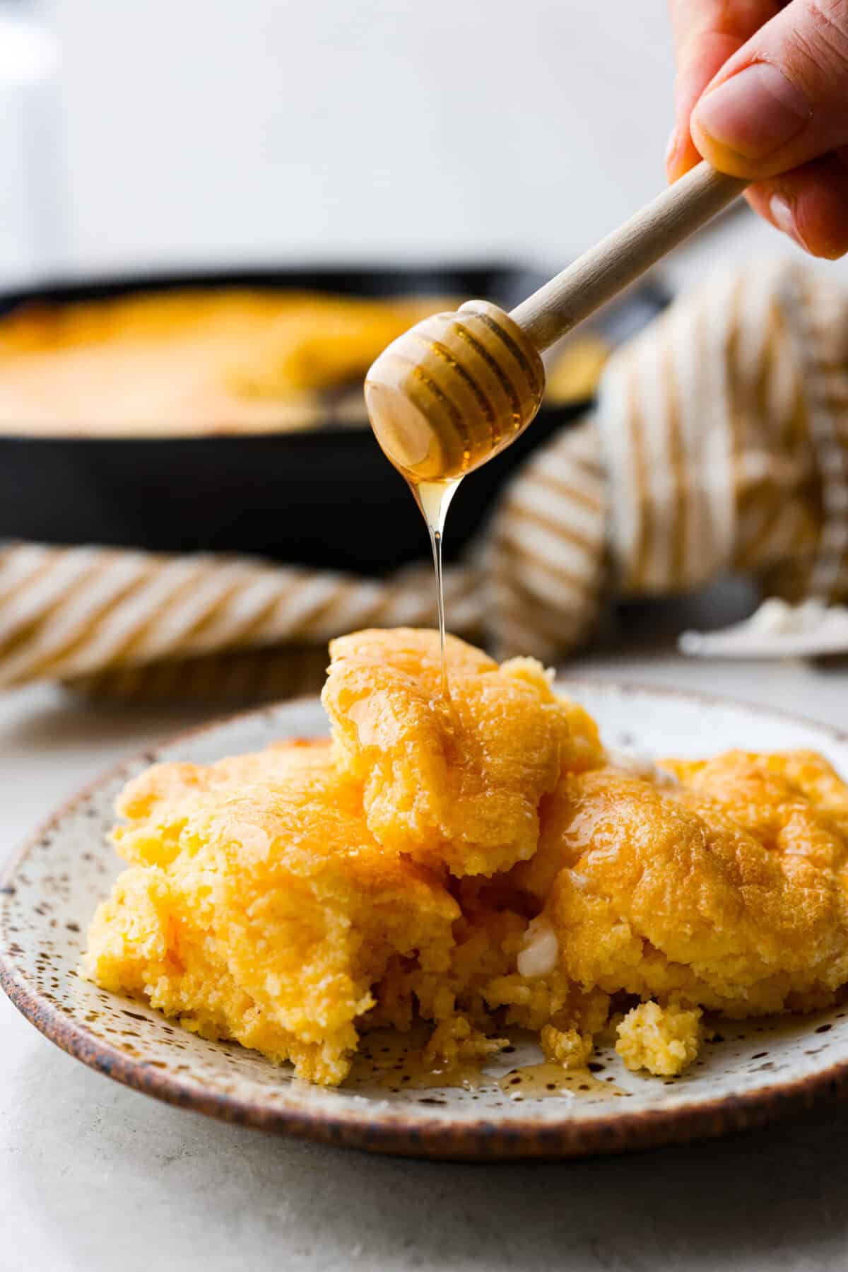 Side shot of a plated piece of spoon bread with honey being drizzled over the top. 