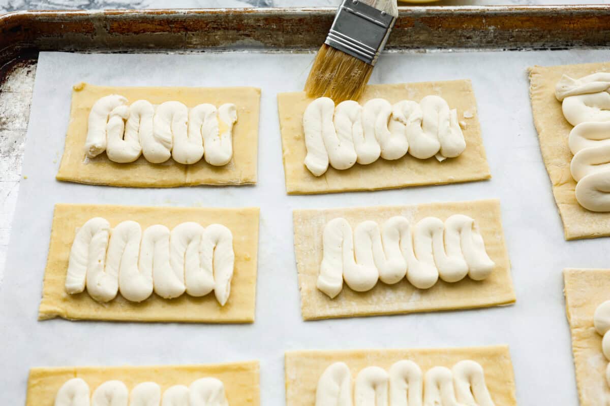 Overhead shot of someone brushing the egg and water mixture on to the exposed puff pastry around the filling. 