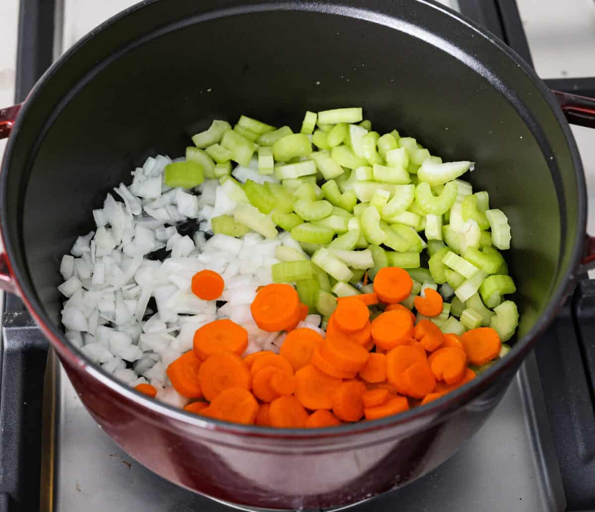 Overhead shot of celery, onions and carrots in a pot with olive oil. 