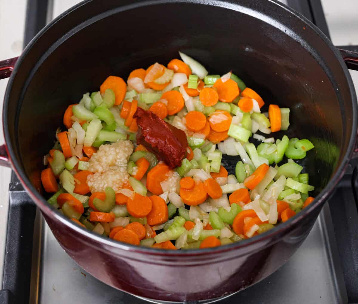 Overhead shot of partially cooked vegetables with garlic and tomato past added. 