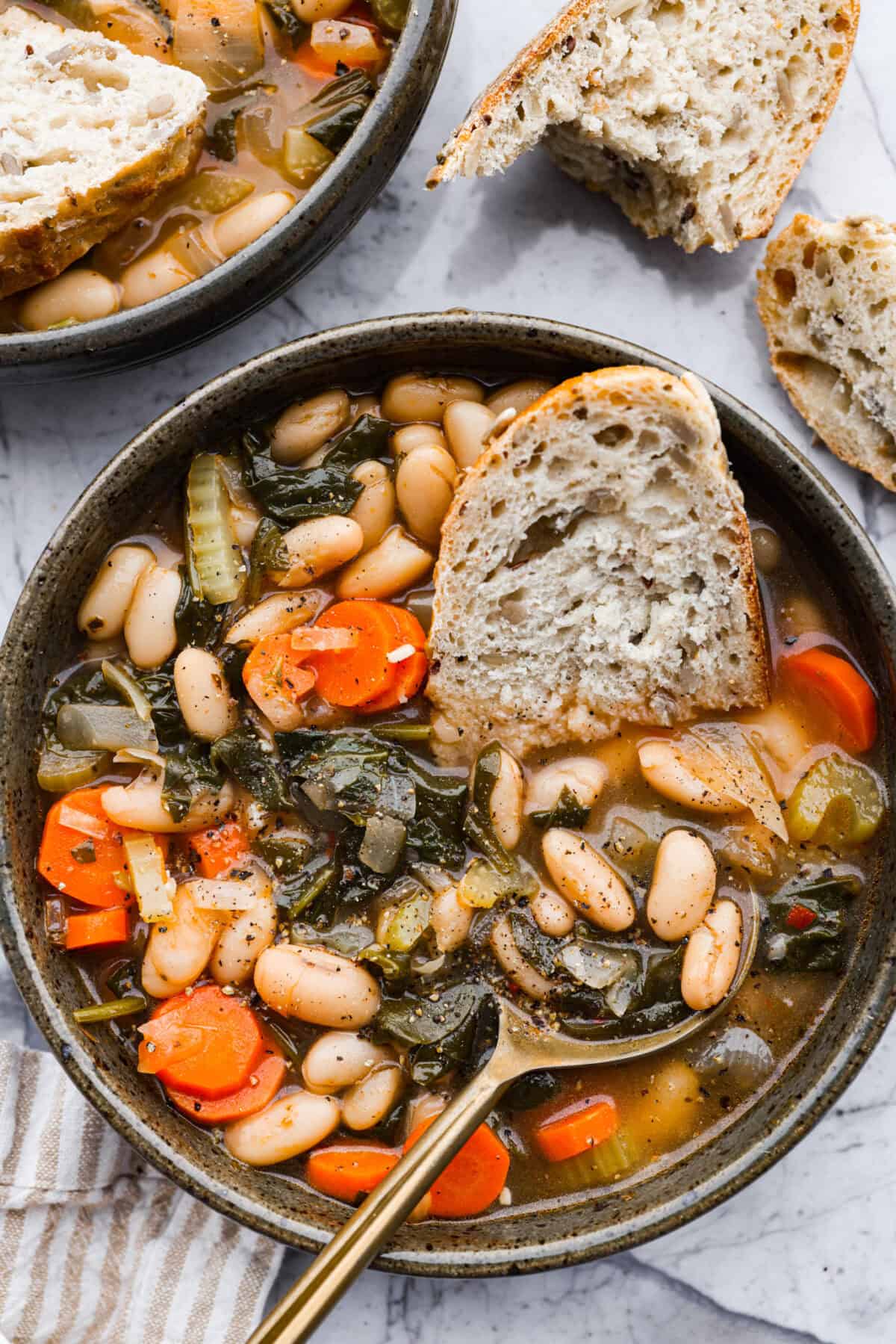 Overhead shot of a bowl of Tuscan white bean soup with a half a slice of bread in it.