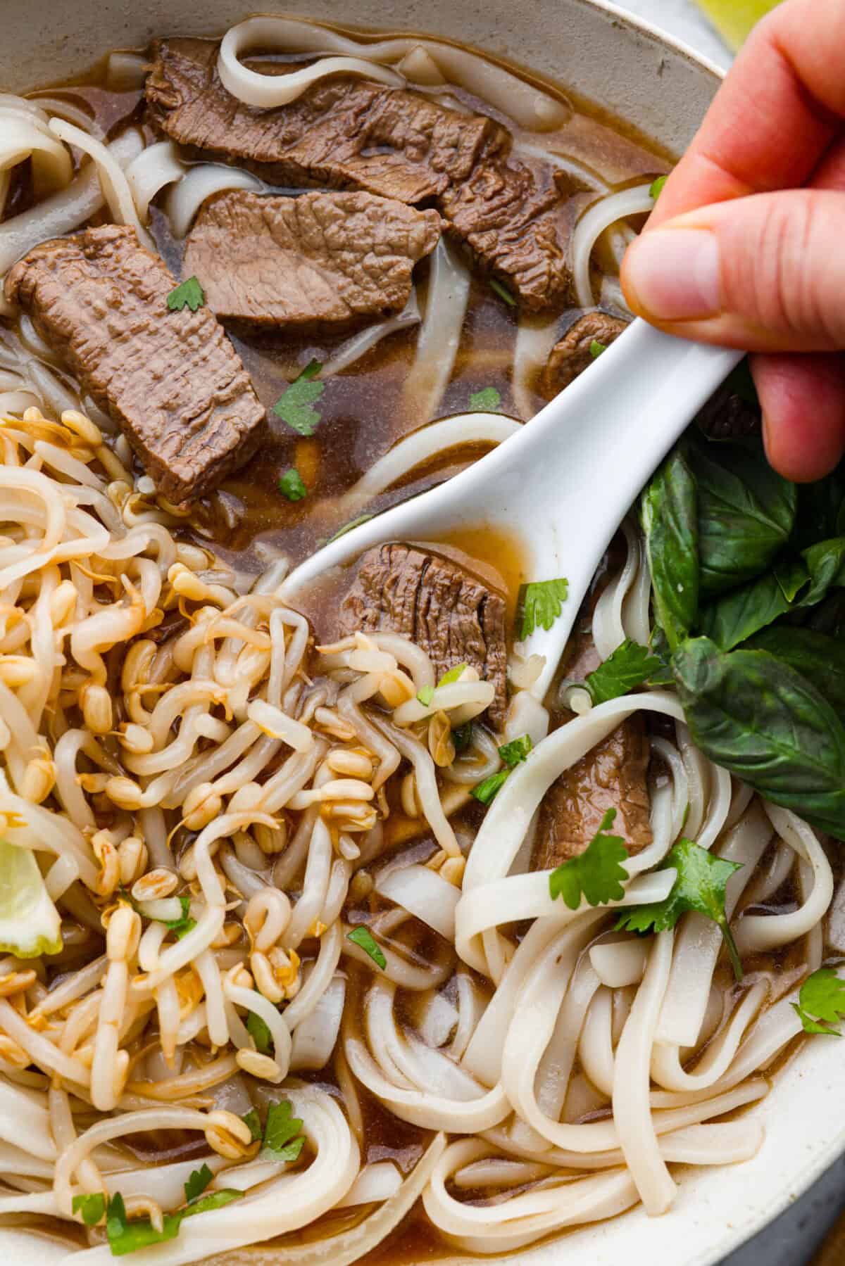 Close up shot of someone getting a spoonful of Vietnamese noodle soup from the bowl. 