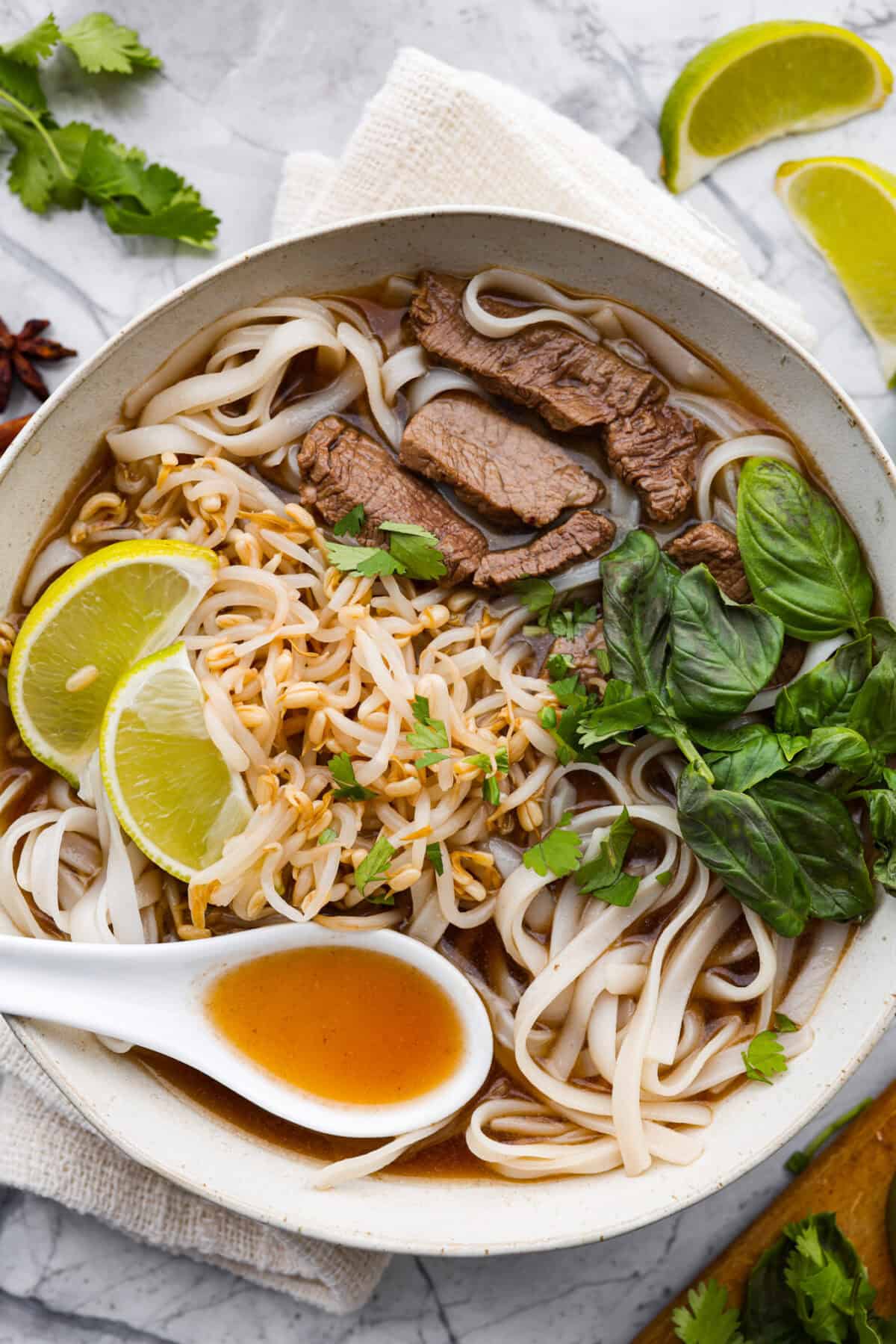 Overhead shot of Vietnamese noodle soup garnished with lime wedges, cilantro and Thai basil. 