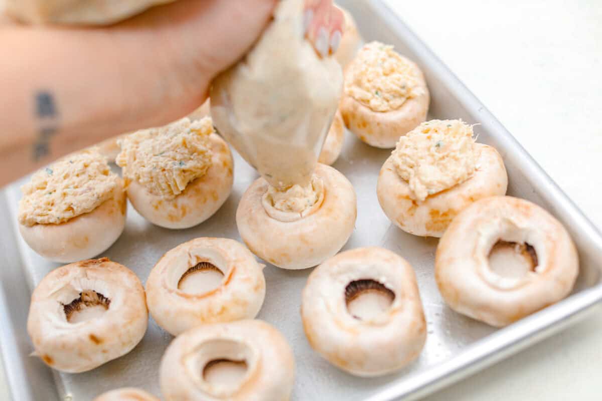 Overhead shot of someone piping crab stuffed mushroom filling into the de-stemmed mushrooms. 