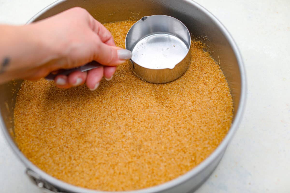 Pressing graham cracker crumbs into a springform pan.