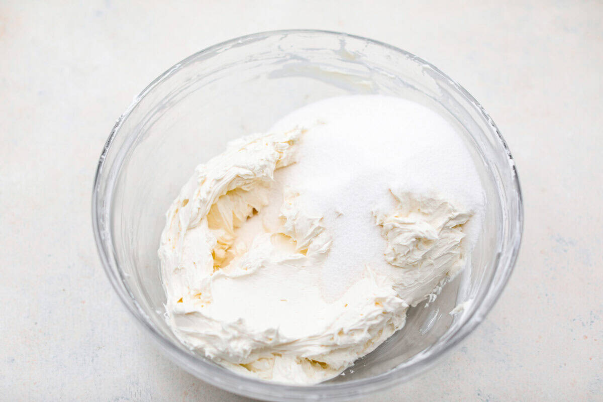 Adding sugar to beat cream cheese in a bowl.