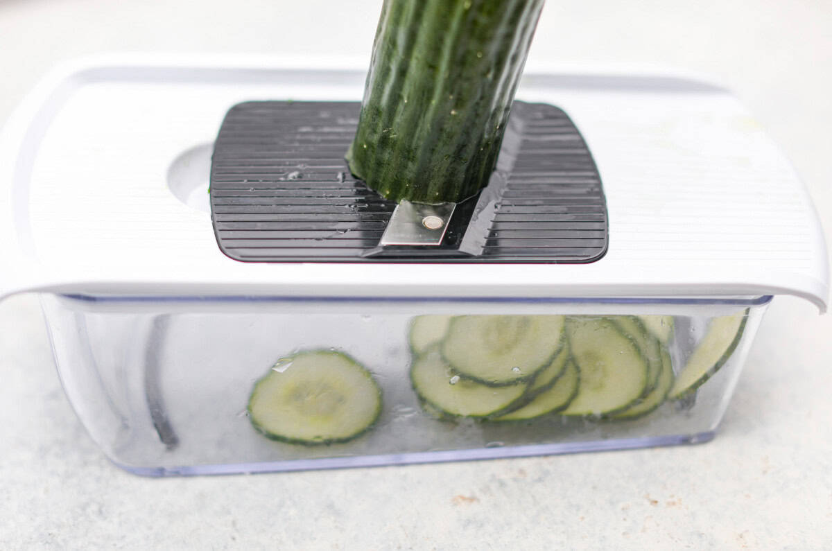 Angles hot of someone slicing a cucumber using a Mandoline. 