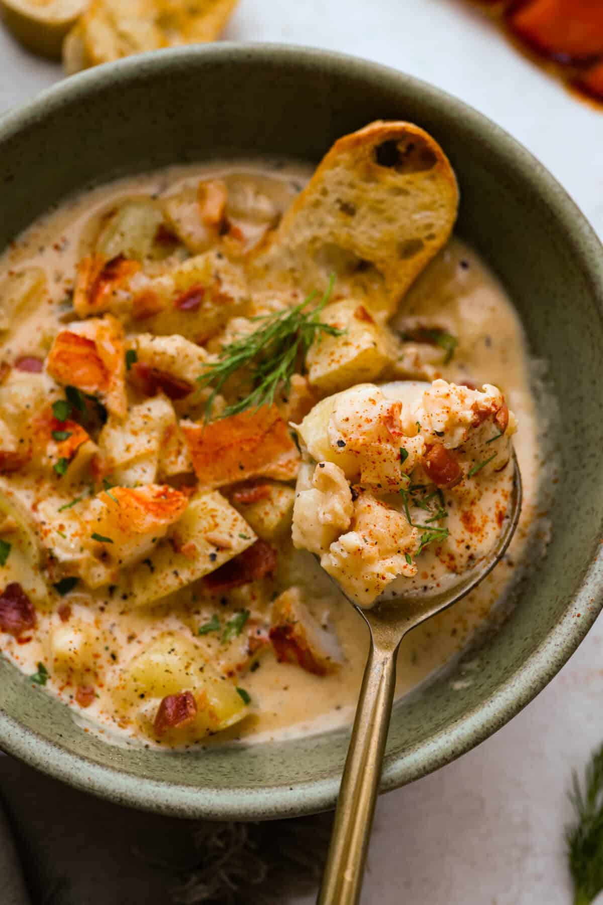 Overhead shot of a spoon with a bite of lobster chowder being held over a bowl of chowder. 