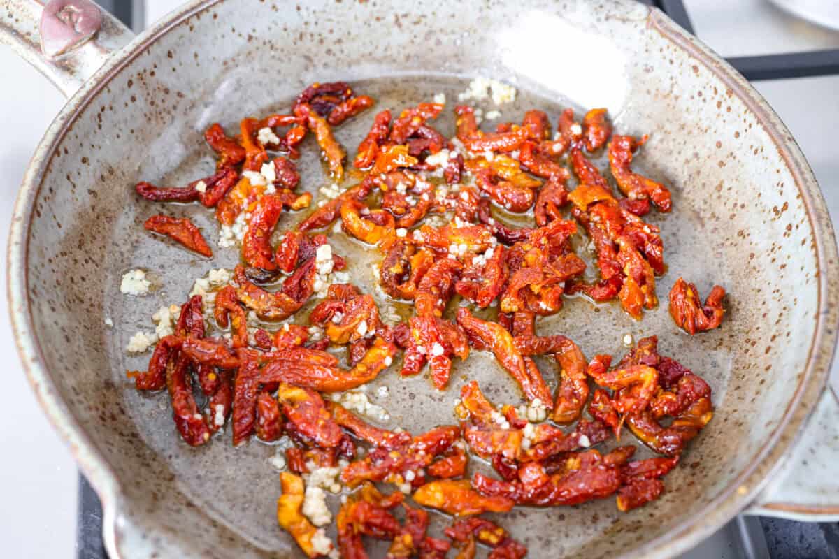 Overhead shot of garlic and sun dried tomatoes in a skillet with olive oil. 