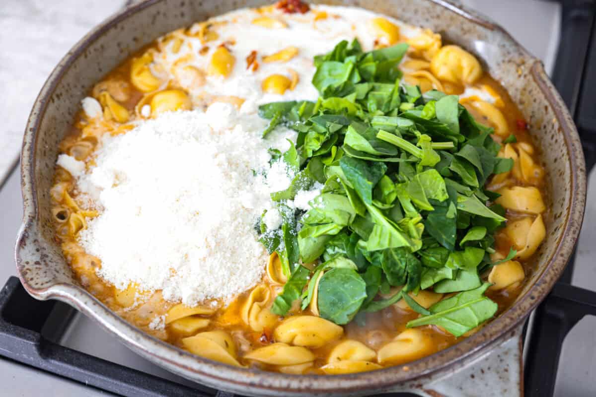 Close up shot of cheese, spinach and cream added to the tortellini and sauce. 