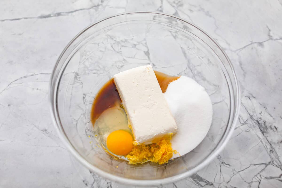 Overhead shot  of cream cheese, egg, lemon zest, sugar and vanilla extract in a mixing bowl. 