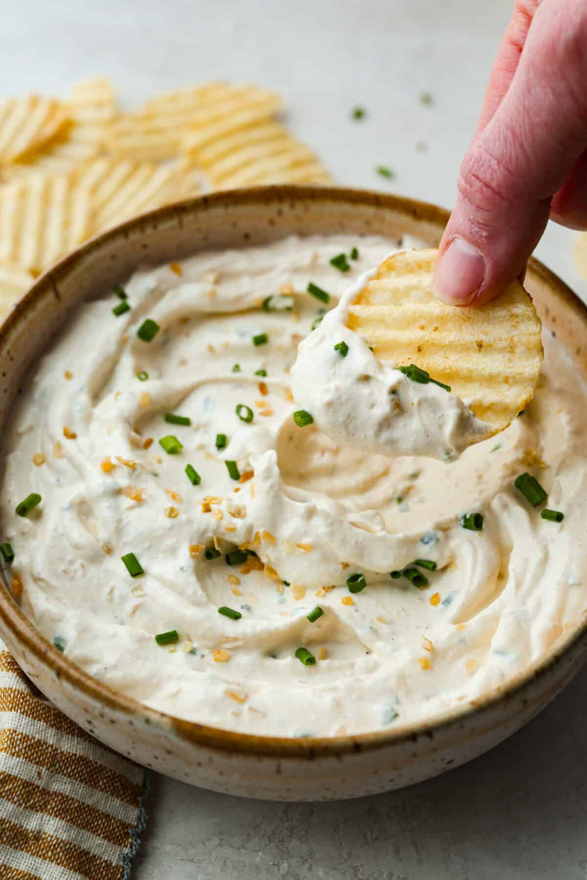 Close up shot of someone scooping a bite of sour cream and onion dip with a chip. 