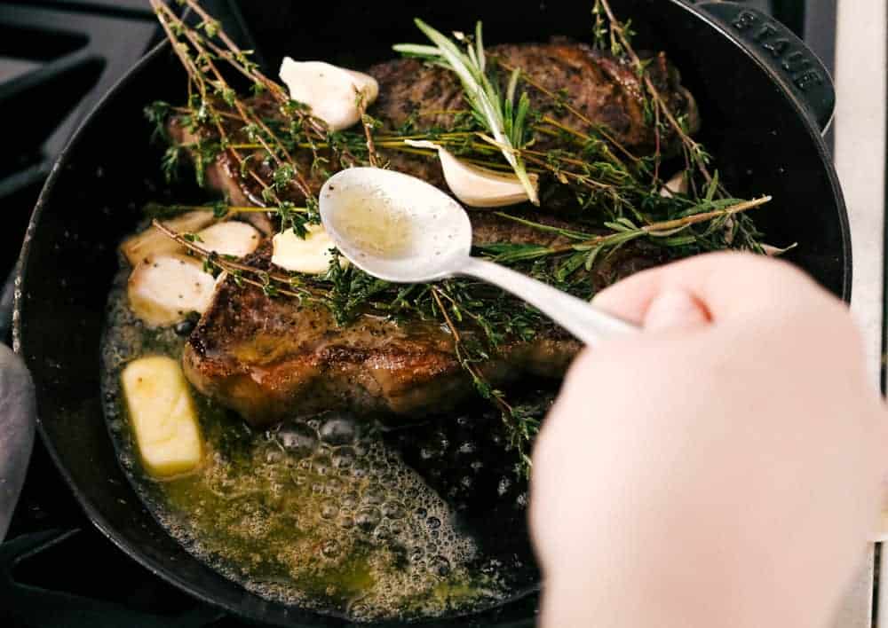 Angle shot of someone basting the steaks with seasoned butter. 