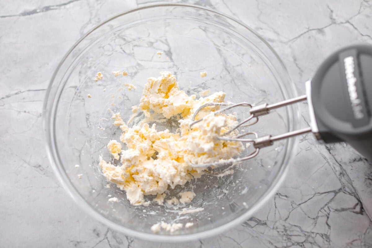 Overhead shot of the cream cheese being beaten with a hand mixer. 