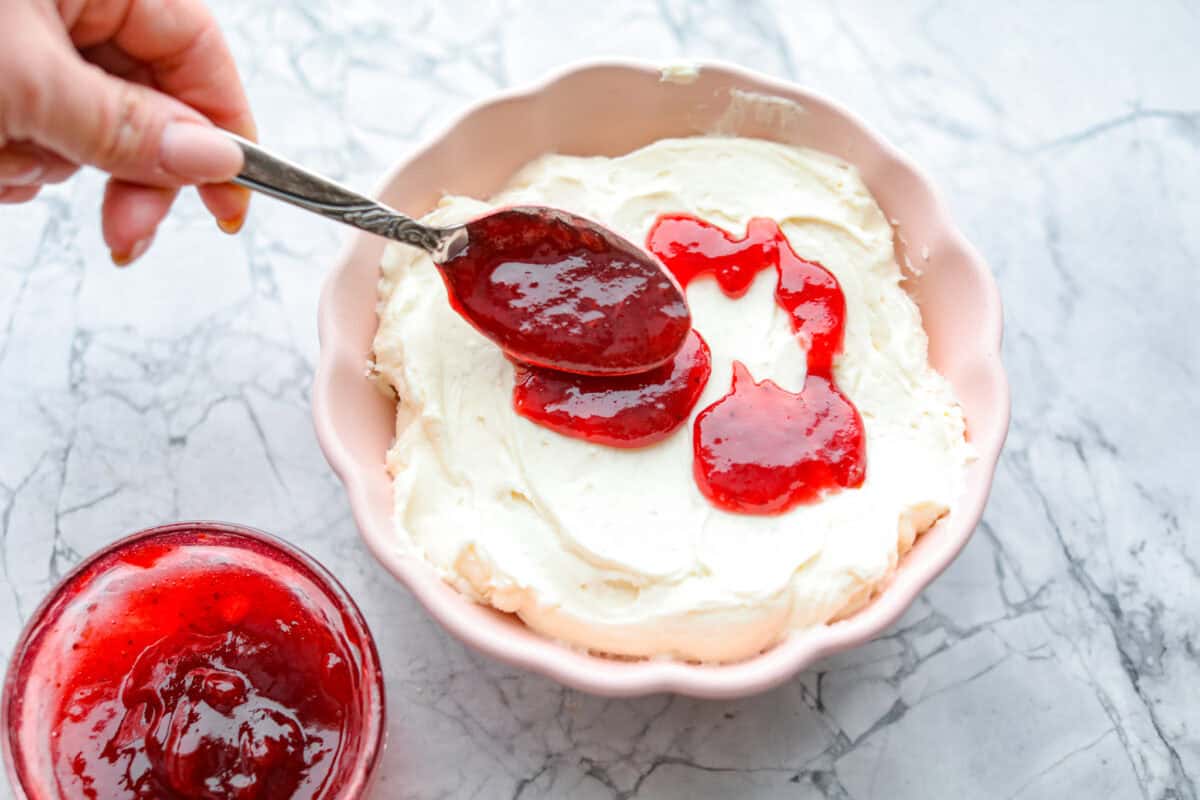 Overhead shot of someone spreading strawberry jam over the cream cheese mixture. 